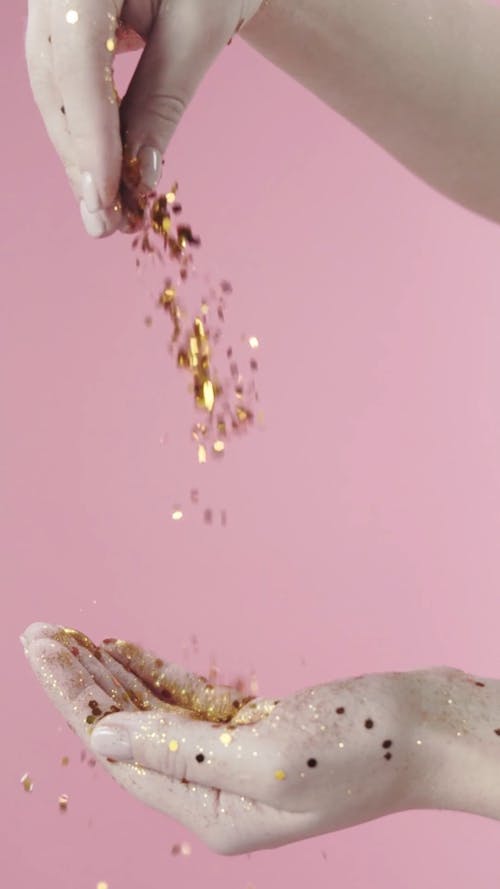Repetitive Footage Of Sprinkling Gold Glitters On A Hand