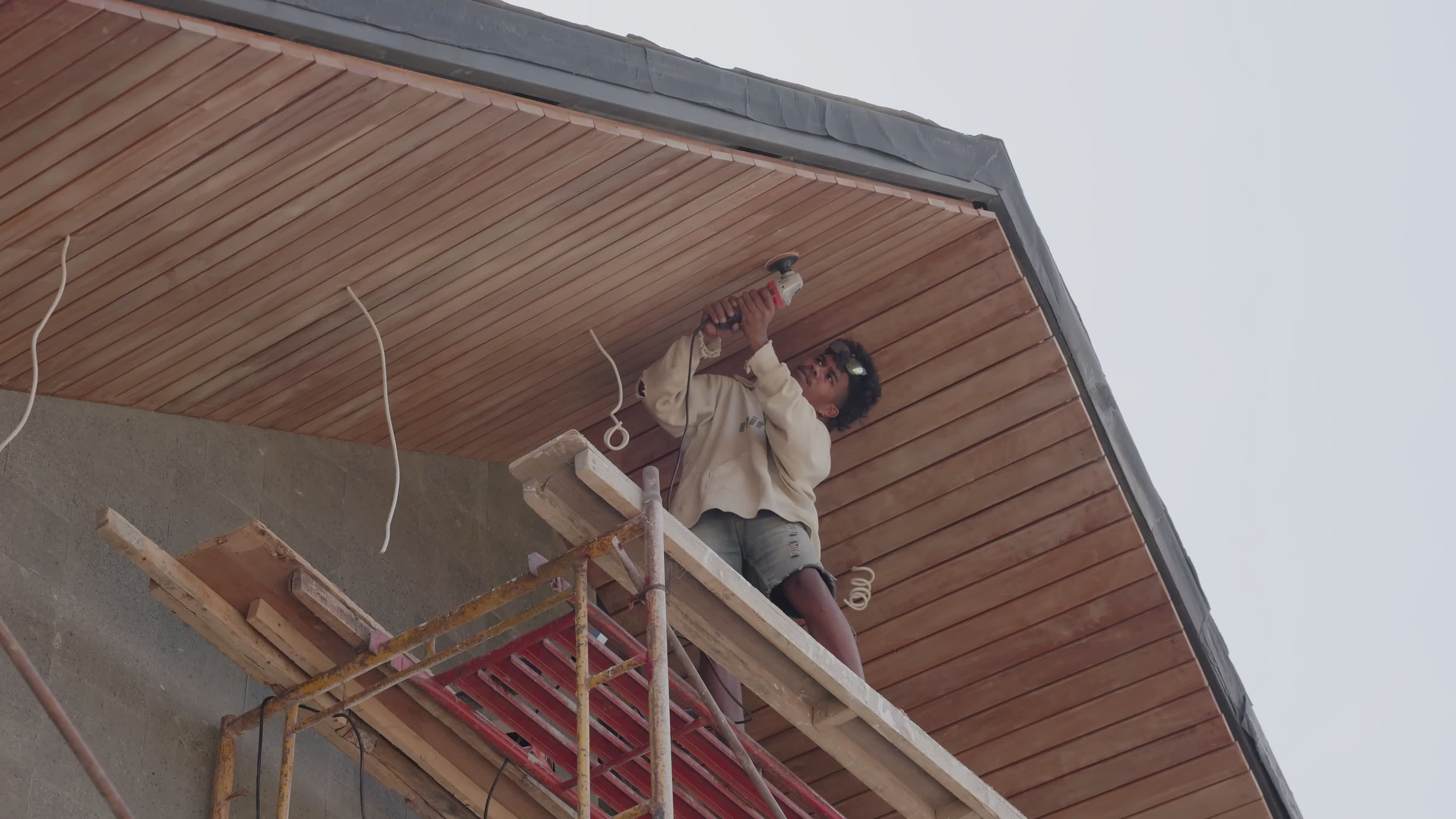 Ridgeline installer securing roof panels from scaffolding on a two-storey home