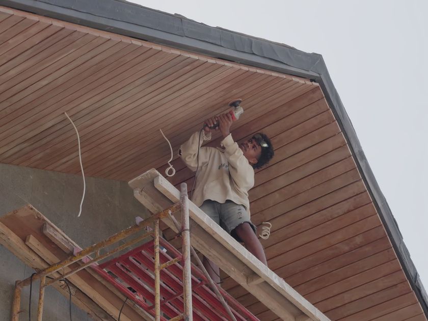 Installer fastening standing-seam metal panels from scaffold