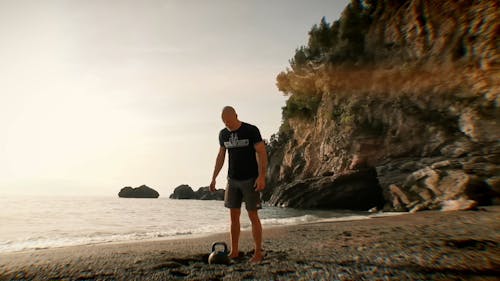 A Man Doing A Kettle Ball Exercise By The Beach