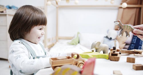 A Kid Happily Playing With Someone With His Wooden Toys