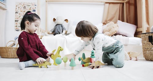 Two Little Kids Playing Wooden Toys On The Floor