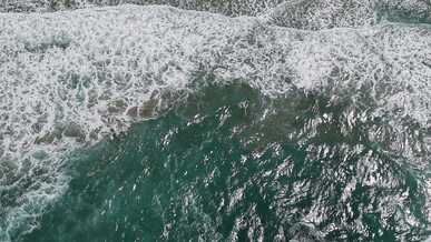 aerial view of ocean waves crashing on sandy beach
