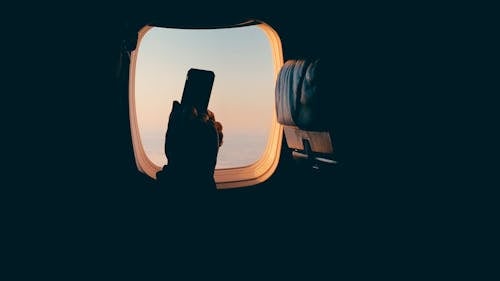 Пассажир самолета с сиденьем у окна пользуется мобильным телефоном в полете