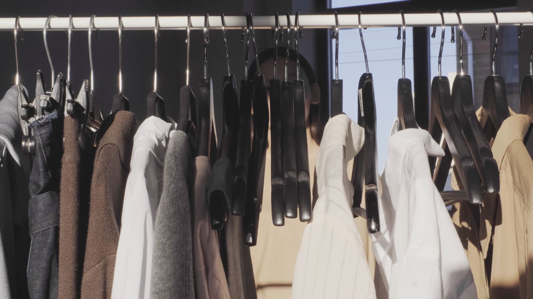 Film still — a woman parting garments on a clothes rail