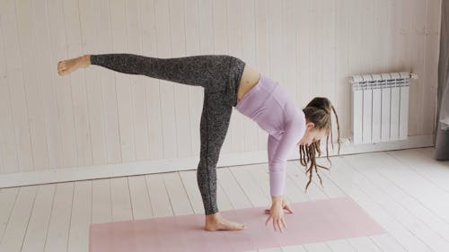 Женщина делает упражнения на растяжку и балансировку над циновкой