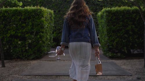 Woman Running With Bottle Of Wine Into The Garden With Hedges