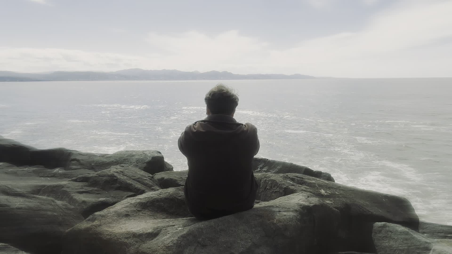 Contemplative Man Sitting by Ocean on Rocky Shore Free Stock Video ...