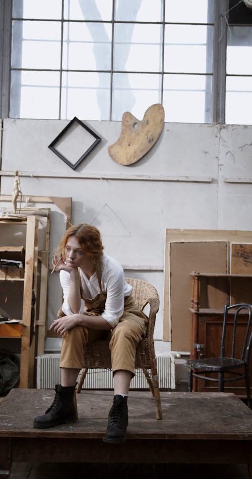 Ein Maler Mit Einem Pinsel Auf Der Hand Ist In Tiefen Gedanken, Während Er Auf Einem Stuhl In Einem Kunststudio Sitzt