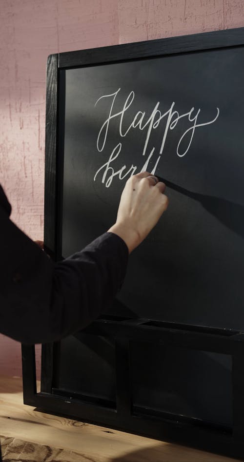 Writing A Birthday Greeting In Calligraphy On A Blackboard Using a Chalk