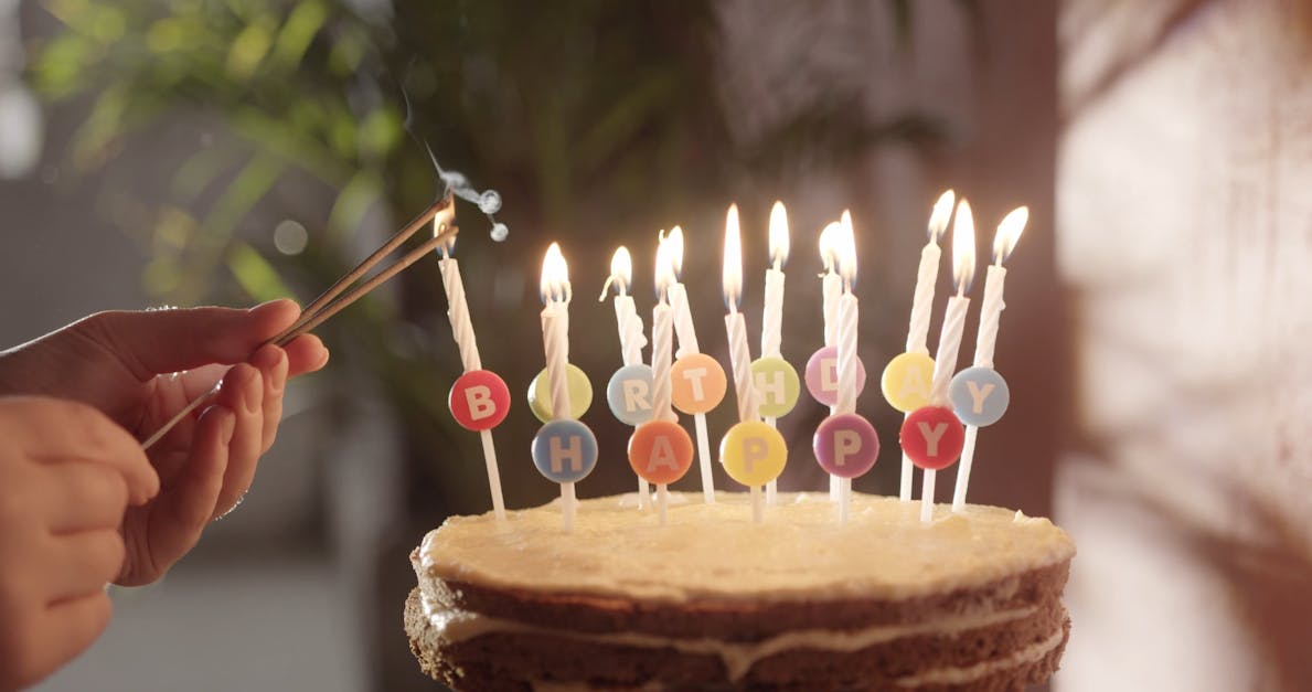 Un pastel de cumpleaños con velas encendidas se ilumina con bengalas en el  fondo.
