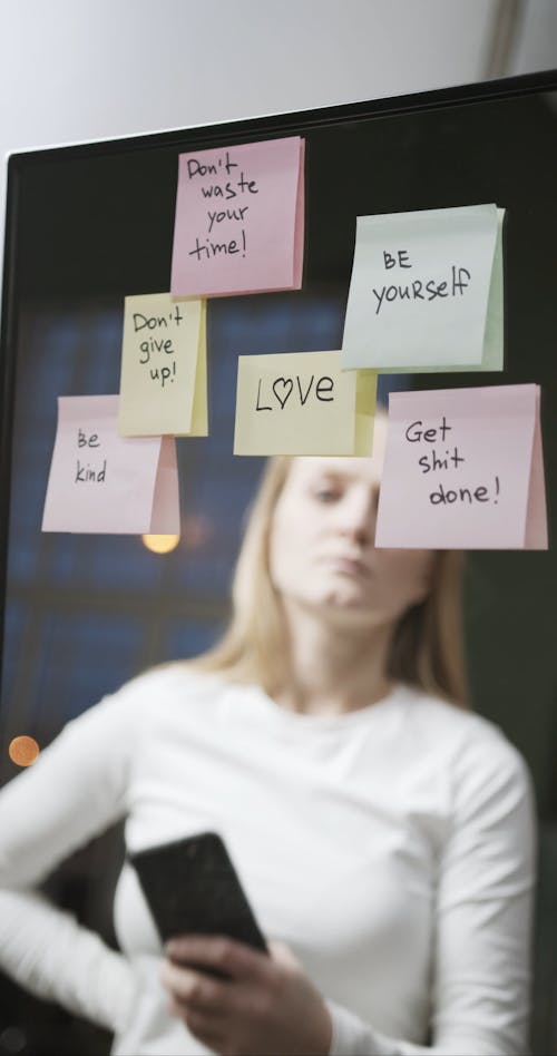 Женщина фотографирует мотивационные слова, написанные на стикерах над зеркалом
