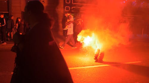 A Man Holding A Lighted Flare While Walking On The Street