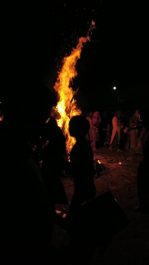A Crowd Of People Walking In Circle Around A Bonfire