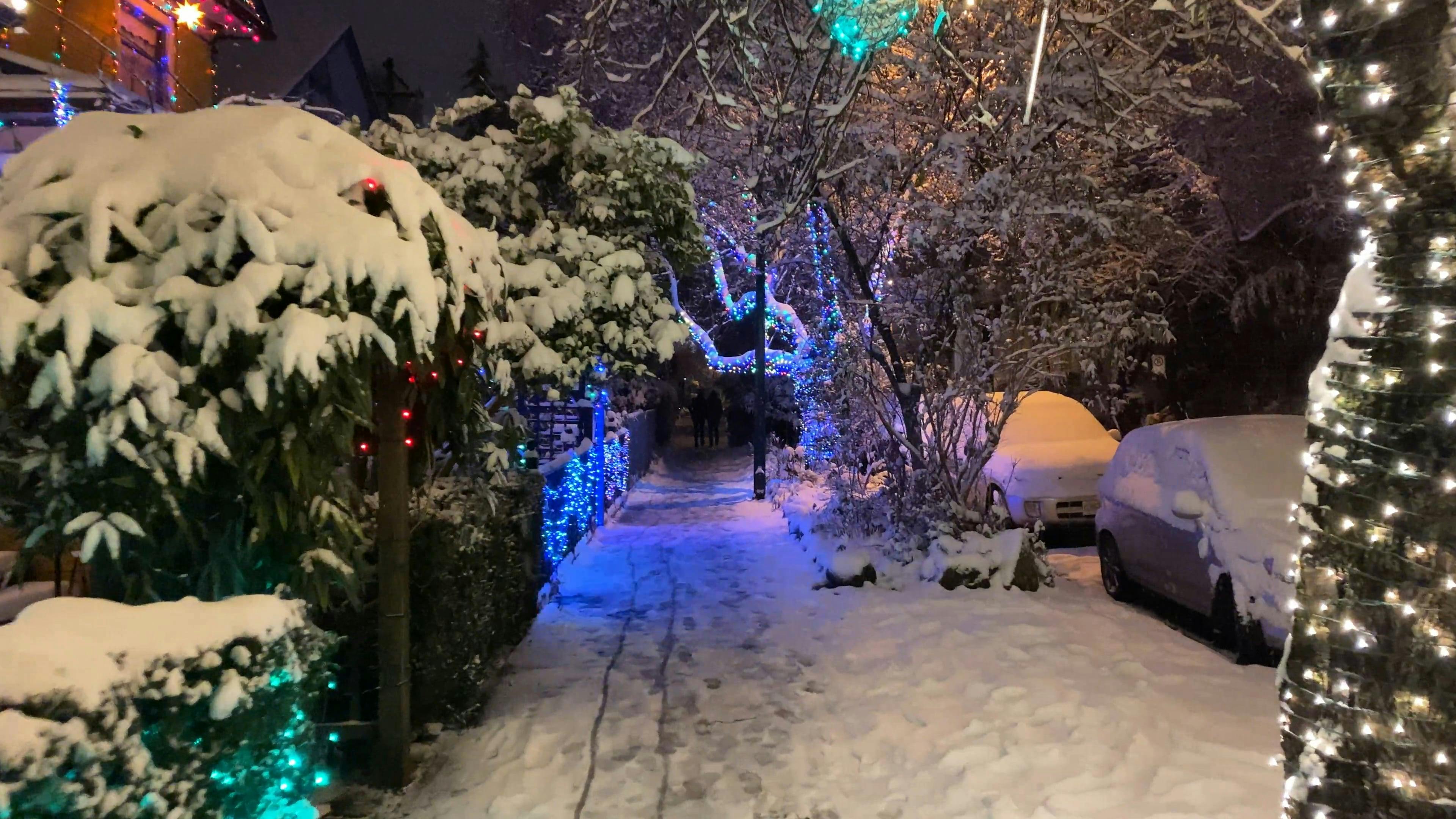 A Sidewalk Covered In Snow Brightened By Christmas Lights Decorations