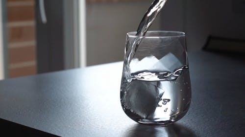 Poring Water On A Glass With Ice Cubes