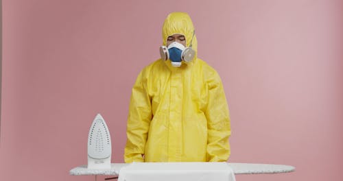 A Man Flat Ironing A Shirt While In Full Protective Gear And Gas Mask