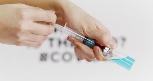 Person Holding A Vaccine With Poster On Background 