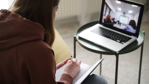 Woman Taking Down Notes While On A Video Conference