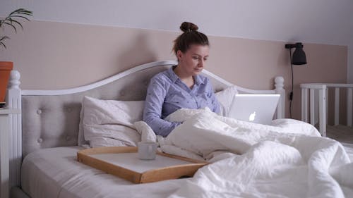 A Woman Working On A Laptop While Staying In Bed