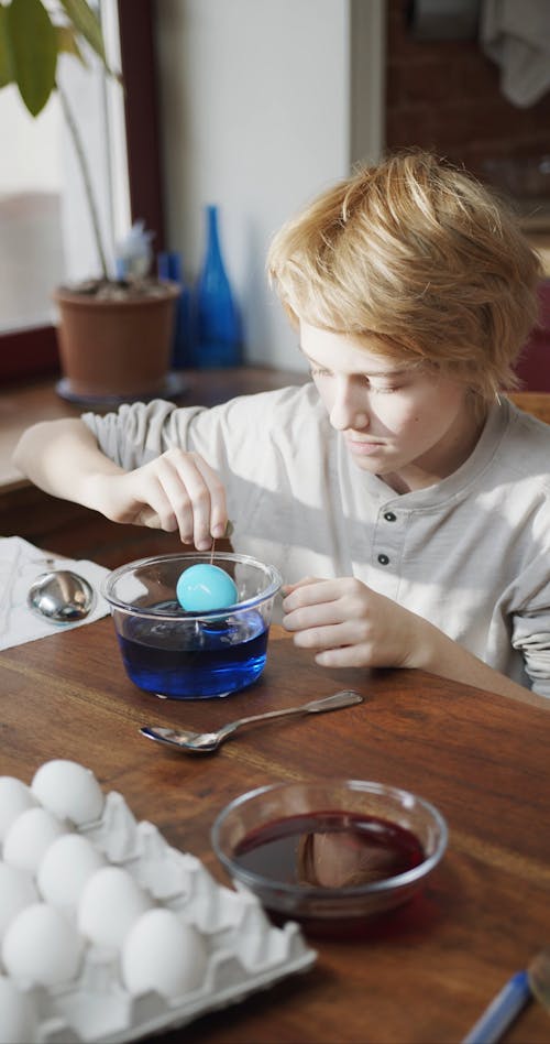 A Boy Scooping Out The Colored Egg From A Bowl Of Color Blue Liquid Coloring