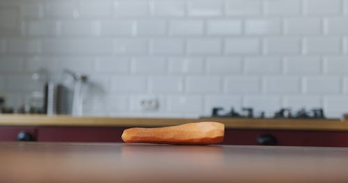 A Girl Sneaking To Grab A Peeled Carrot Lying Over The Kitchen Table