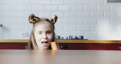 A Girl Goofing Around The Kitchen Table With Carrots On Hand 