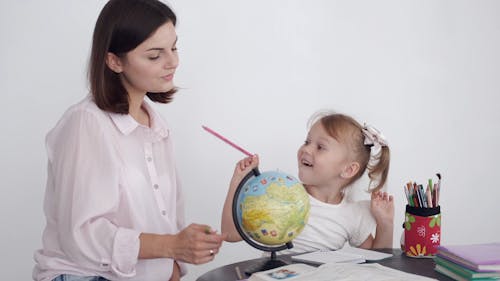 A Mother Teaching Her Daughter Geography Using A Globe