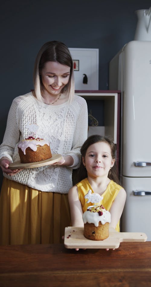 A Mother And Daughter Holding Easter Cakes Set On  Wooden Boards