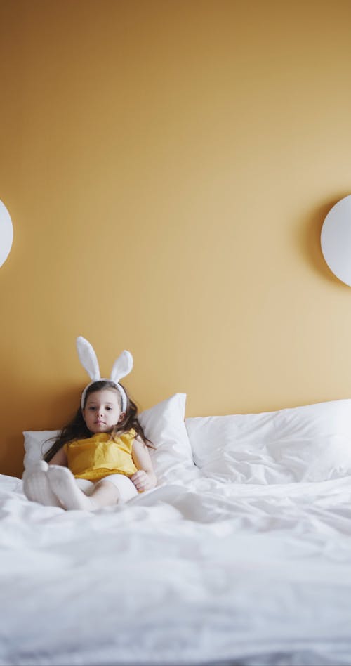 A Girl Laying On A Bed Wearing An Easter Bunny Headband 