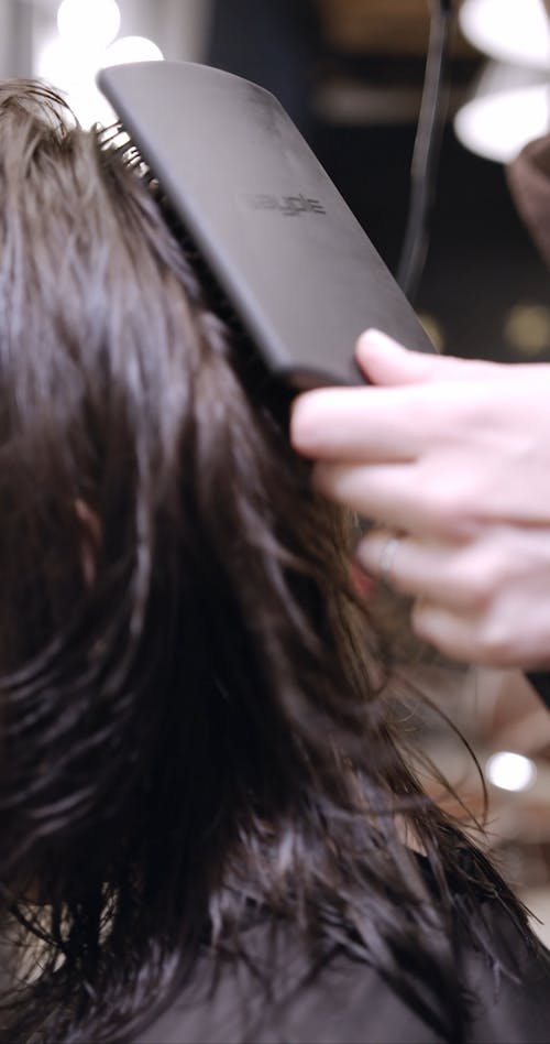 A Hairdresser Brushing While Blow Drying A Woman's Hair