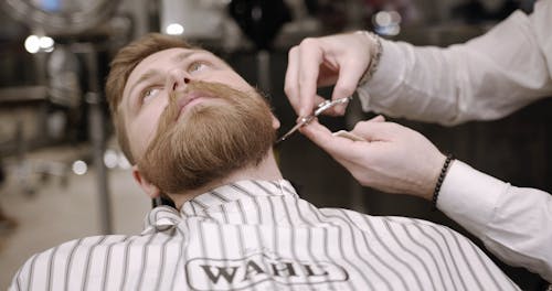 A Barber Using A Scissor In Trimming A Man's Beard