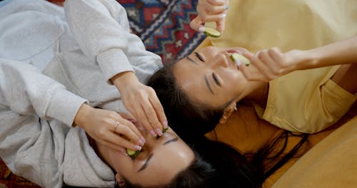 Two Women Placing Slice Cucumbers Over Their Eyes