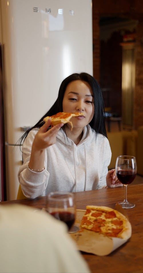 A Woman In White Hoodie Sweat Shirt Eating A Slice Of Pizza