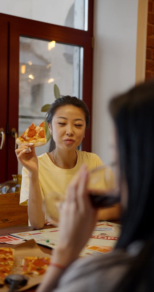 Two Women Eating Pizza With Red Wine While Playing A Game Of Monopoly