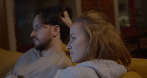 A Woman Rubbing Her Partner's Hair While They Are Watching Television In The Living Room