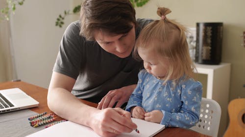 A Father Showing His Daughter How to Draw With Crayons
