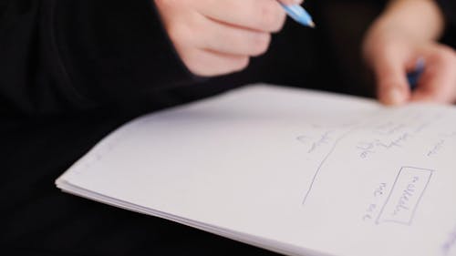 Close-up View Of A Person Writing On A Notebook