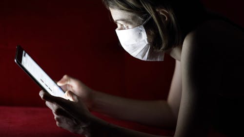 A Woman Wearing A Face Mask While Using An Ipad