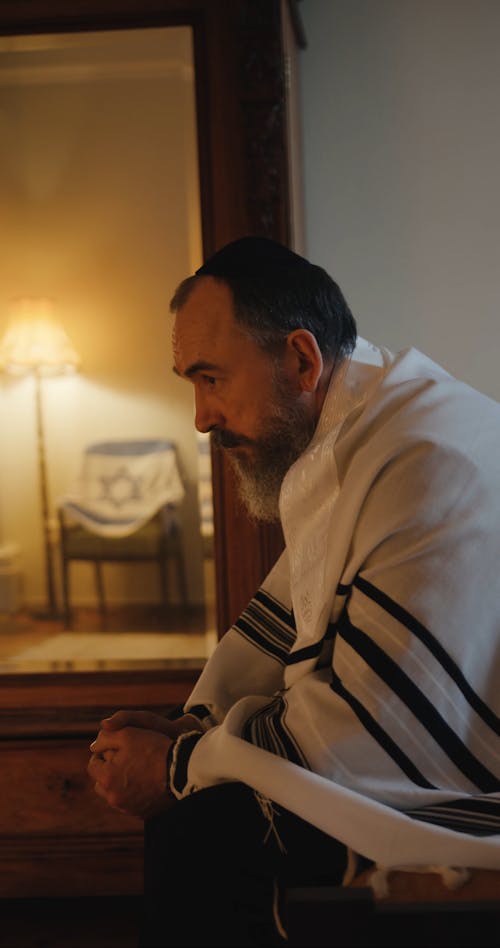 A Jewish Man Wearing Tallit Looking At Himself On A Mirror
