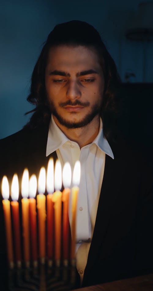 A Man Sitting Behind The Burning Candles On A Hanukkiah