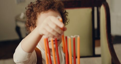 A Boy Sticking Candles On A Hannukiah