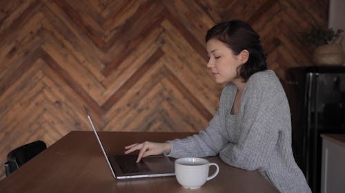 A Woman Typing on a Laptop while Drinking Coffee