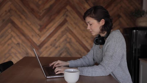 a Woman Typing on a Laptop while Drinking Coffee and Listening to Music