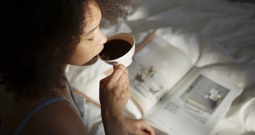 A Woman Reading A magazine While Having Coffee In Bed