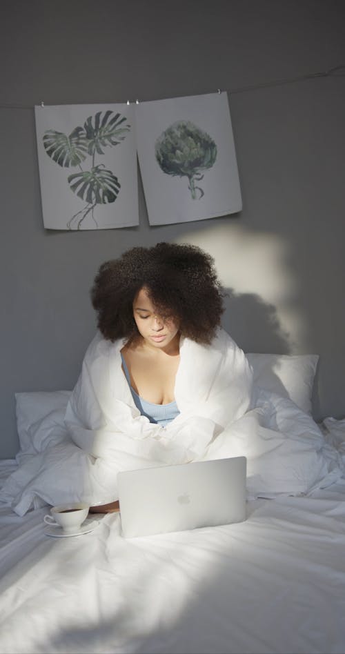 A Woman Using Her Laptop While Having Coffee In Bed