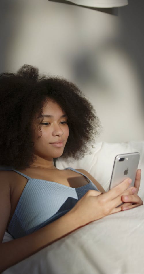 A Woman Using Her Cellphone While Lying In Bed