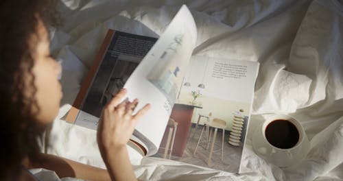 A Woman Having Coffee In Bed While Looking At A Magazine