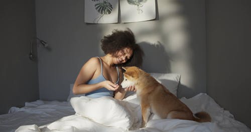 A Woman Teasing Her Pet Dog With Food While In Bed