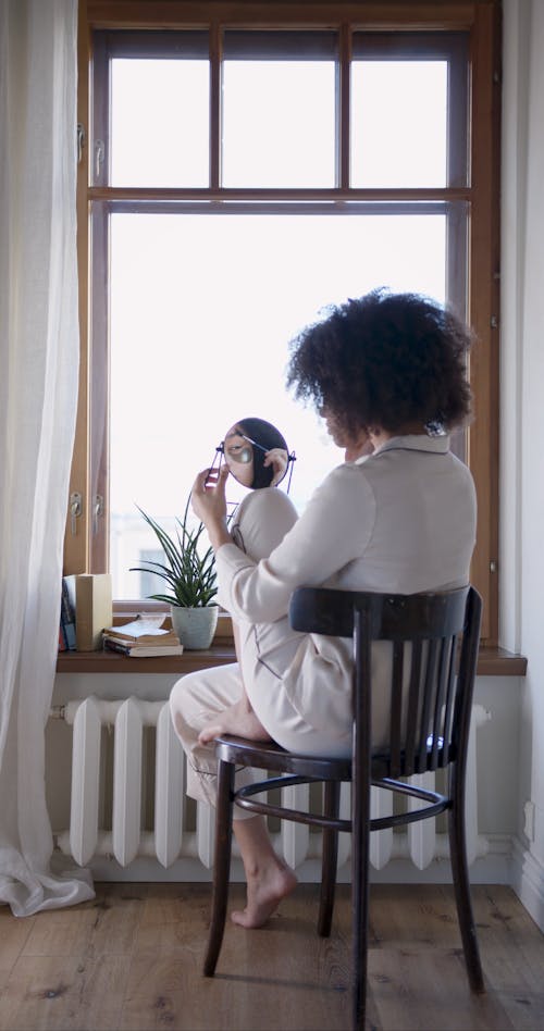 A Woman Doing Her Eye Brow By The Window
